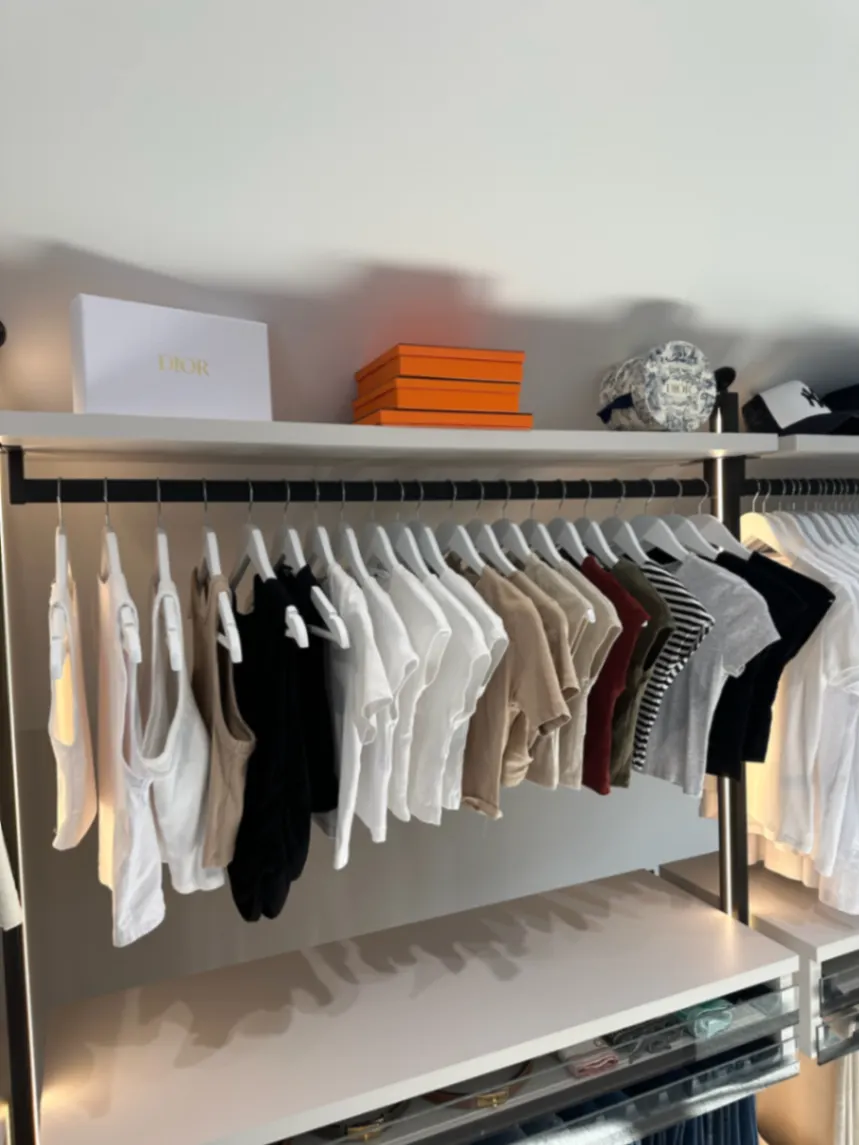 Clothes grouped on a light wardrobe rail with accessories above