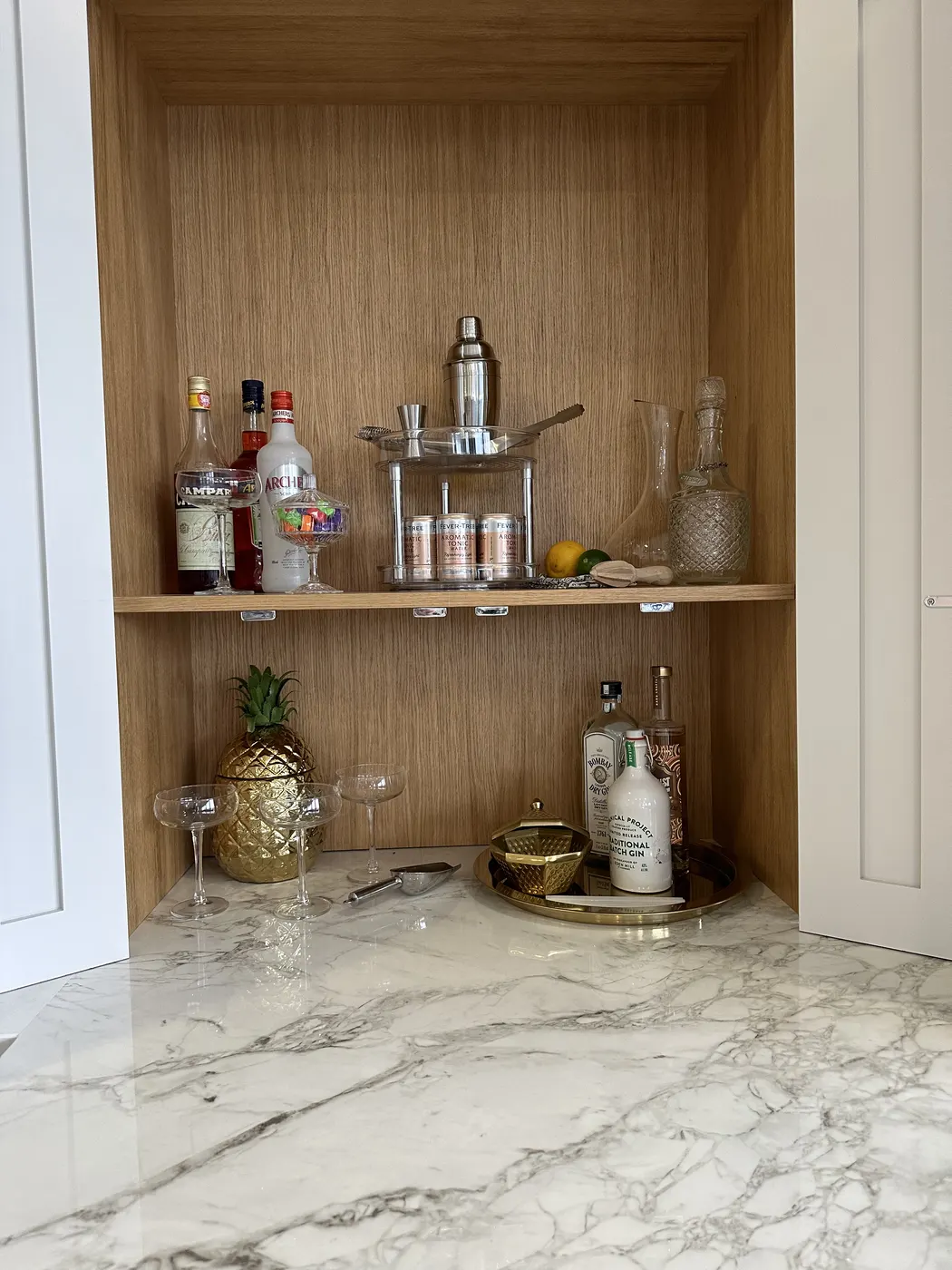 Drinks cupboard with glasses and bottles arranged on oak shelves