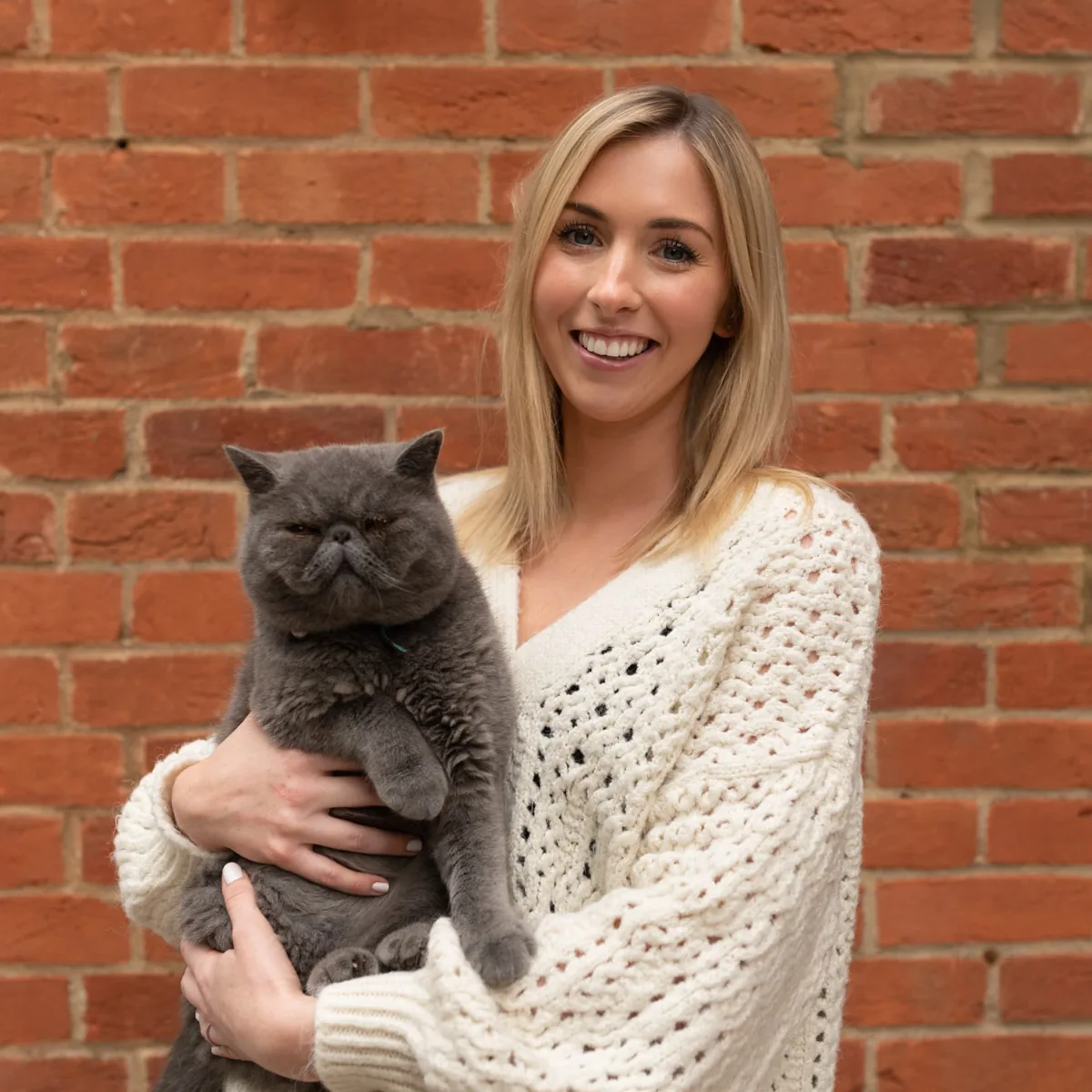 Ruth holding a grey cat beside a brick wall