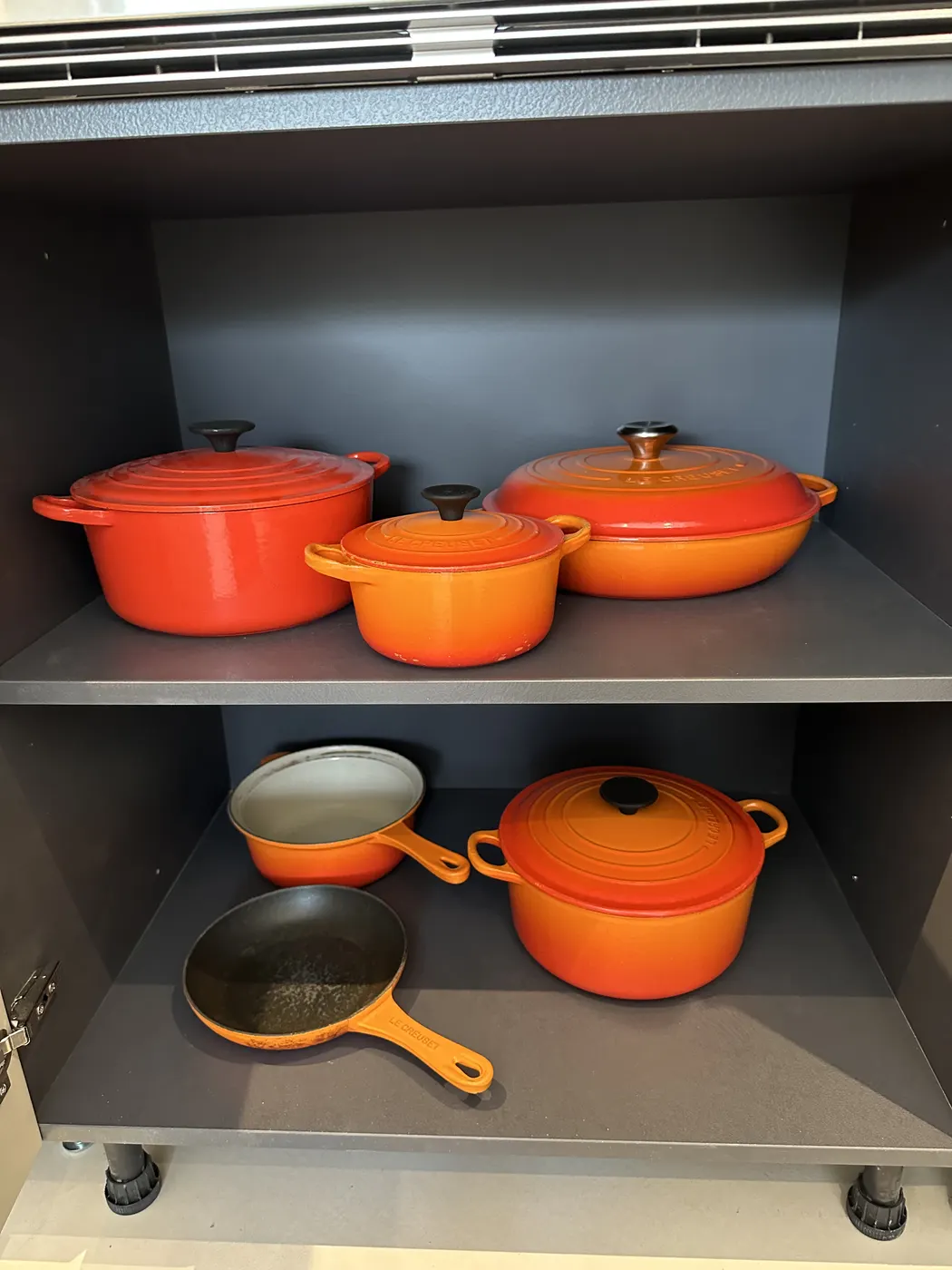 Orange cast-iron pans stacked neatly in a deep kitchen drawer