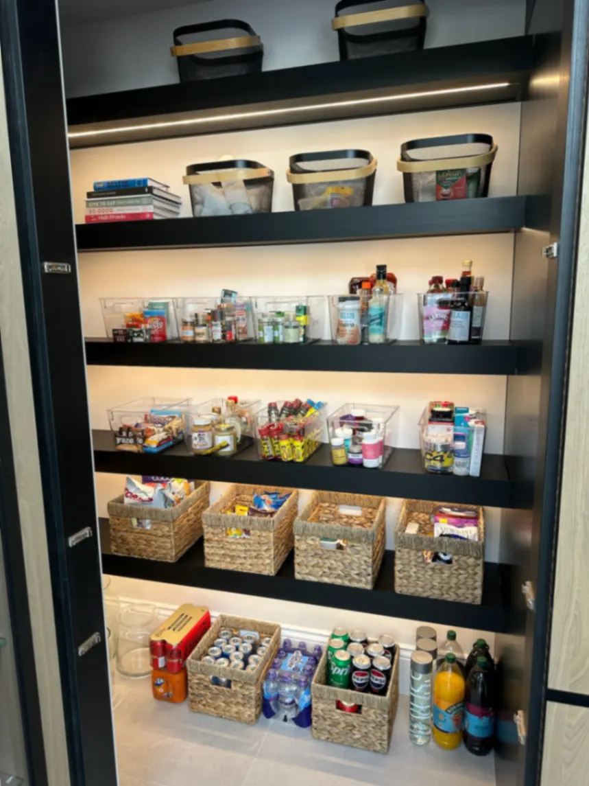Food and drinks grouped on pantry shelves with baskets above