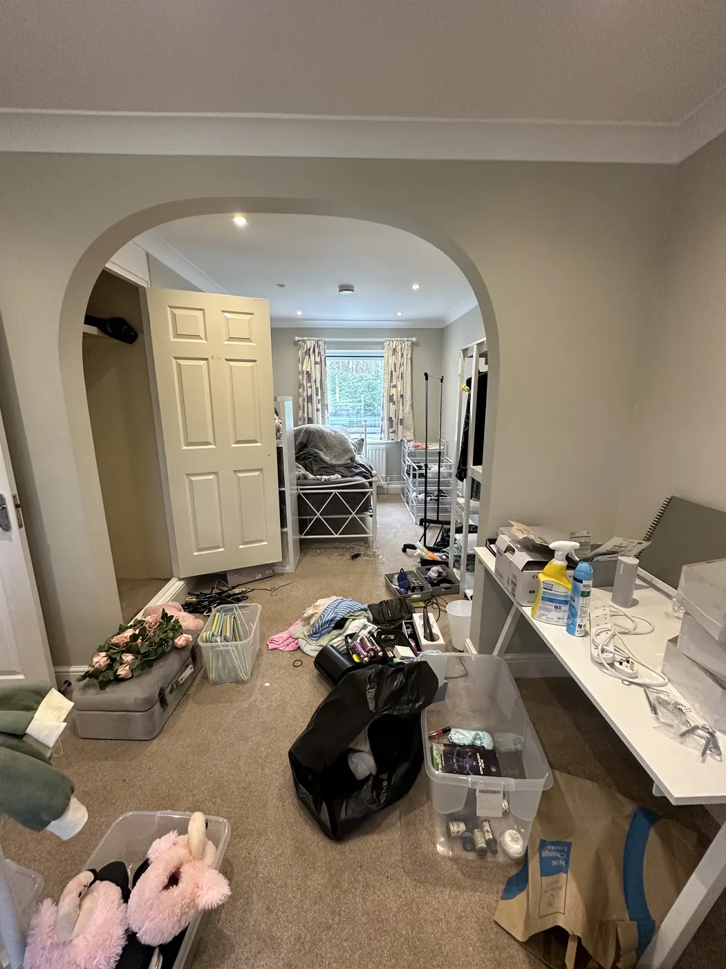 Bedroom through an archway before, with clothes and bags across the floor